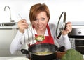 Happy home cook woman in red apron at domestic kitchen holding saucepan with soup tasting delicious vegetable stew