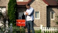 Happy house owner looking at for sale signboard against house, moving concept