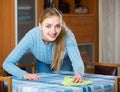 Happy housewife in sweater dusting table in living room