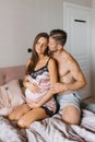 Happy husband and a pregnant wife are sitting on the bed on a day off in the morning . A man embraces a young woman Royalty Free Stock Photo