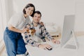 Happy husband and wife pose near computer, keyboard and surf information, work in domestic atmosphere with dog, pose in coworking