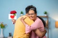 Happy indian adult son hugging or embracing to senior mother by giving red roses with greeting card at home - Royalty Free Stock Photo