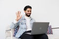 Happy indian business man in casual making video call from home couch, looking at camera, smiling, waving hand hello, attending Royalty Free Stock Photo