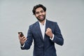 Happy indian business man holding cell phone celebrating win isolated on beige.