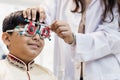 Happy Indian child boy examining eyesight modern ophthalmology equipment in clinic. Patient kid male checkup iris examines