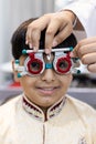 Happy Indian child boy examining eyesight modern ophthalmology equipment in clinic. Patient kid male checkup iris examines