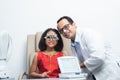 Happy Indian child girl doing examine eyesight with trial frame and lens with ophthalmologist or optometrist for eyes test