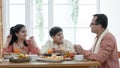 Happy Indian family enjoy eating food with hands, South Asian father and children wear traditional clothes, sitting at table