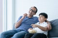 Happy Indian father and child son laughing and eating popcorn, watching funny comedy movie tv show, sitting on sofa, Indian family Royalty Free Stock Photo