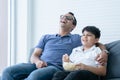 Happy Indian father and child son laughing and eating popcorn, watching funny comedy movie tv show, sitting on sofa, Indian family Royalty Free Stock Photo