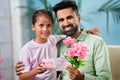 Happy indian girl kid giving gift with flowers to father by looking at camera at home - concept of fathers day, family Royalty Free Stock Photo
