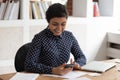 Smiling indian girl distracted from studying using cellphone Royalty Free Stock Photo