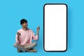 Happy indian guy pointing at huge smartphone with blank screen