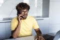 Happy indian guy having conversation on phone, using laptop at kitchen Royalty Free Stock Photo