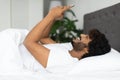 Happy indian guy lying in bed, using smartphone, side view Royalty Free Stock Photo