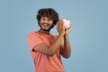 Happy indian man holding piggy bank next to ear Royalty Free Stock Photo