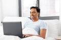 Happy indian man with laptop in bed at home Royalty Free Stock Photo