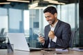 Happy Indian man sitting at a desk in the office in front of a laptop with a wad of money in his hands, happy to win Royalty Free Stock Photo