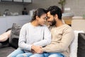 Happy Indian newlyweds moved in new apartment, sitting at the sofa in embraces, looking at each other. Multi ethnic