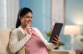 Happy indian pregnant woman greeting on video call to doctor using digital tablet from home - concept of online Royalty Free Stock Photo