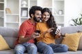 Happy Indian Spouses Browsing Modern App On Smartphone While Relaxing At Home