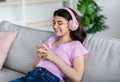 Happy Indian teen girl wearing headphones, using mobile phone, listening to music or audio book, communicating online