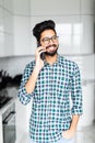 Happy indian young man in checkered shirt talking on cell phone on the kitchen Royalty Free Stock Photo