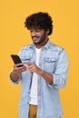 Happy indian young man using cell phone isolated on yellow background.