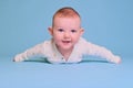 Happy infant baby boy smiling lying on his tummy, blue studio background. Four month old child close up Royalty Free Stock Photo