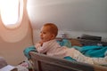 Happy infant baby lyes in special bassinet in airplane at his stomach. First flight of the baby, she is impressed and smiles.