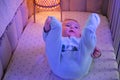 Happy infant baby is playing with leg in the evening bed. Smiling child in turquoise clothes in the light of a night lamp, age six