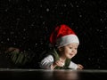 Happy infant boy toddler in red Santa hat and white - green clothes is lying on floor looking at copy space under snow Royalty Free Stock Photo