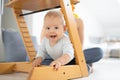 Happy infant climbing under traditional scandinavian designer wooden high chair and in modern bright home. Cute baby Royalty Free Stock Photo