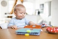 Happy infant sitting at dining table and playing with his toy in traditional scandinavian designer wooden high chair in