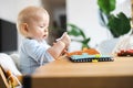 Happy infant sitting at dining table and playing with his toy in traditional scandinavian designer wooden high chair in