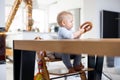 Happy infant sitting at dining table and playing with his toy in traditional scandinavian designer wooden high chair in