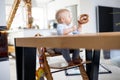 Happy infant sitting at dining table and playing with his toy in traditional scandinavian designer wooden high chair in