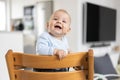 Happy infant sitting in traditional scandinavian designer wooden high chair and laughing out loud in modern bright home Royalty Free Stock Photo