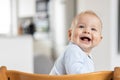 Happy infant sitting in traditional scandinavian designer wooden high chair and laughing out loud in modern bright home Royalty Free Stock Photo