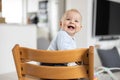 Happy infant sitting in traditional scandinavian designer wooden high chair and laughing out loud in modern bright home Royalty Free Stock Photo