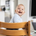 Happy infant sitting in traditional scandinavian designer wooden high chair and laughing out loud in modern bright home Royalty Free Stock Photo