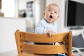 Happy infant sitting in traditional scandinavian designer wooden high chair in modern bright home. Cute baby. Royalty Free Stock Photo