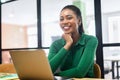 Happy inspired African-American female office employee using laptop computer indoors, resting chin with hand and looking Royalty Free Stock Photo