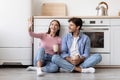 Happy inspired caucasian young couple with cups of coffee watching at free space, sit on floor