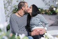 Happy international couple in striped sweaters is kissing, muslim man hugging belly of his pregnant wife while sitting on the bed Royalty Free Stock Photo