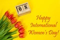 Happy International Women`s Day composition bouquet of red tulip buttons, wooden cubic calendar and greeting text. Flat lay from