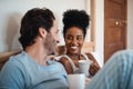 Happy interracial couple, bed and coffee in relax for morning, bonding or breakfast at home. Man and woman smiling for Royalty Free Stock Photo