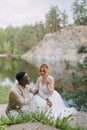 Happy interracial couple newlyweds sits and has a fun near dandelions against background of lake, forest and canyon Royalty Free Stock Photo