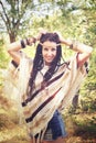 Happy joyful boho style woman outdoor portrait, dressed in knitted poncho and headband, posing hands up against sunny park Royalty Free Stock Photo