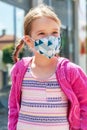 Happy joyful little girl, school age child wearing a protective face mask smiling, portrait, vertical. Kid in a colorful facemask